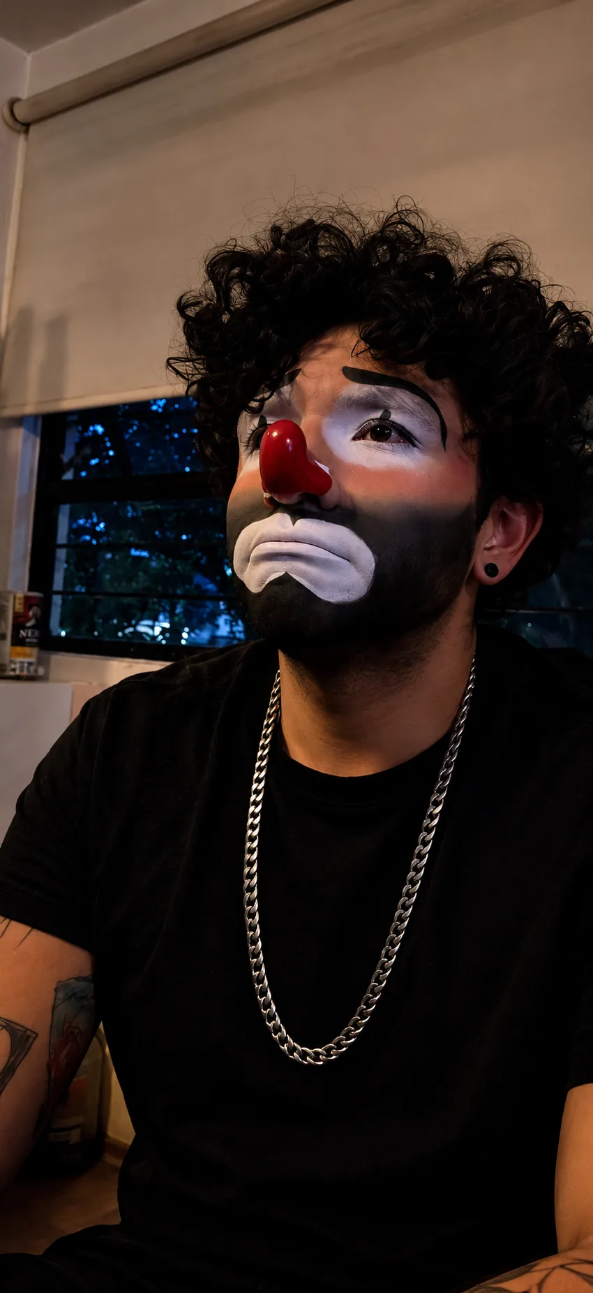 Juan maquillado de payaso triste junto a una ventana